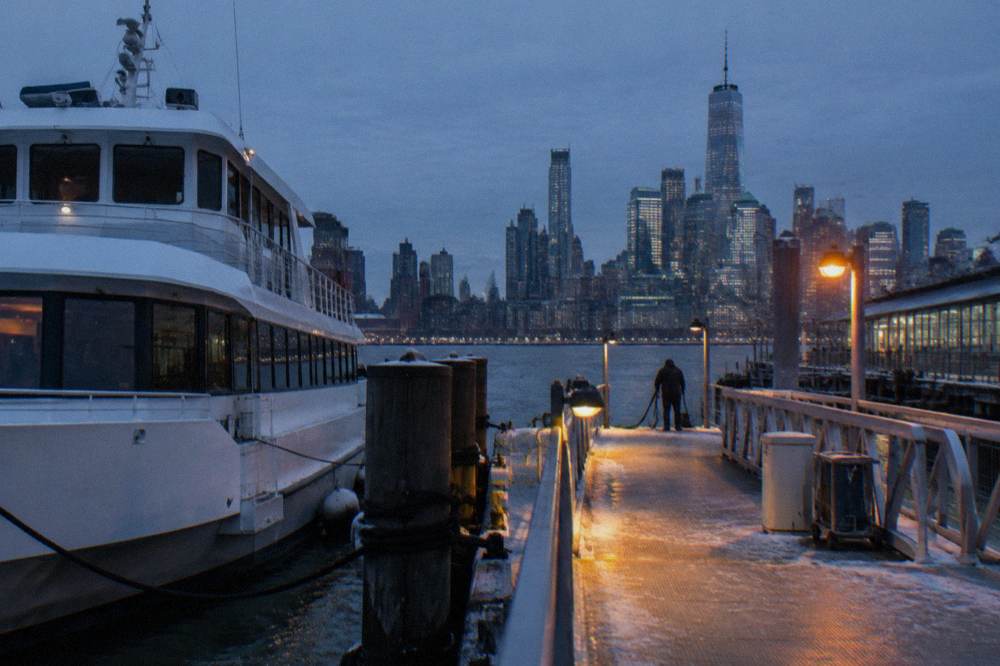 A sightseeing cruise boat docked at a Manhattan pier on the Hudson River at dusk