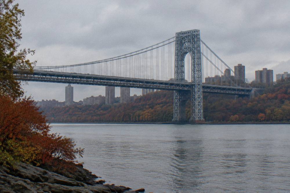 Autumn trees in red and orange along the Hudson River shoreline with calm water in the foreground