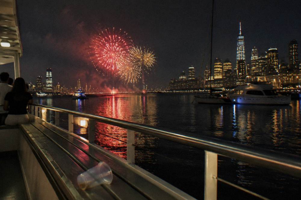 Fireworks bursts reflected in a calm river between city lights at night